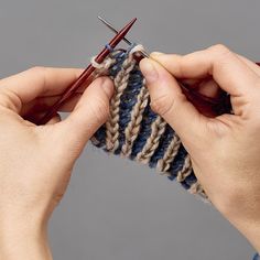 two hands holding knitting needles over a knitted object