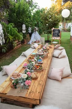 a long wooden table topped with lots of food on top of a lush green field