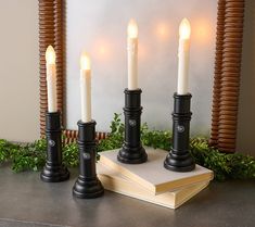 four lit candles sitting on top of a book next to some books and greenery