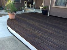 a wooden deck in front of a house with potted plants on the side walk