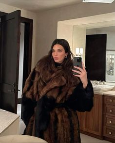 a woman is taking a selfie in the mirror while wearing a fur coat and holding a cell phone