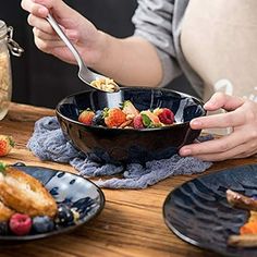 a person eating food from a bowl on top of a wooden table next to other plates