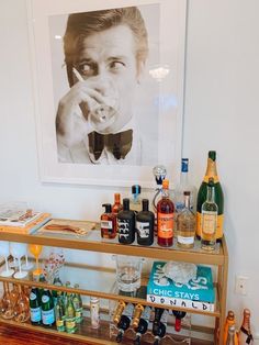 a bar cart with liquor bottles and glasses on it in front of a framed photo