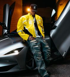 a man sitting on the hood of a sports car with his hands in his pockets