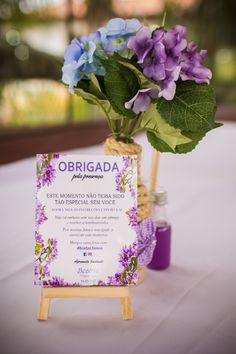 purple and blue flowers are in a vase on a white table cloth with a sign that says obrigada