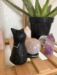 a black cat figurine sitting on top of a wooden shelf next to crystals