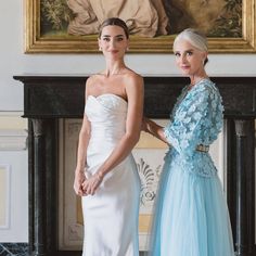 two beautiful women standing next to each other in front of a painting on the wall