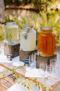 three jars filled with liquid sitting on top of a wooden table next to glasses and bottles