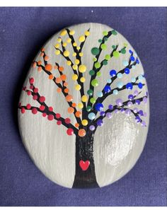 a painted rock with a tree on it and hearts in the middle, sitting on a purple surface