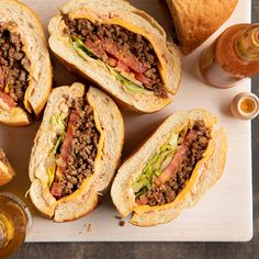 a cutting board topped with cut in half sandwiches next to two glasses of beer and bread