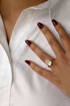 a woman's hand wearing a white shirt and maroon nails with a gold ring