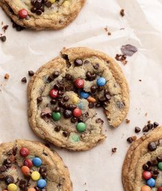 chocolate chip cookies with m & m's and candy chips on top, sitting on parchment paper