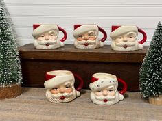 four ceramic santa mugs sitting on top of a wooden table next to christmas trees