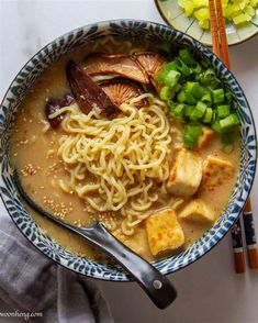 a bowl filled with noodles, tofu and green onions next to chopsticks