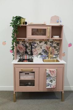 a pink play kitchen with flowers on the wall and potted plant next to it