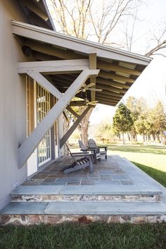 two chairs sitting on the front porch of a house with an awning over it