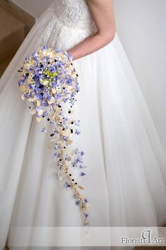 a woman in a white wedding dress holding a bouquet of blue and yellow flowers on her arm