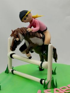 a cake shaped like a girl riding a horse jumping over an obstacle with the word love spelled in pink