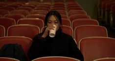 a woman sitting in an empty auditorium drinking from a cup