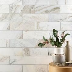 a vase with some flowers in it on a table next to a wall that has white marble tiles