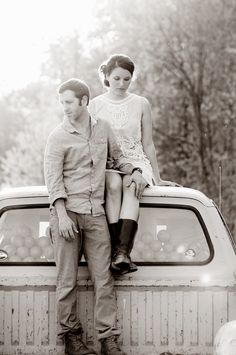 a man and woman sitting on the back of a pick up truck in black and white