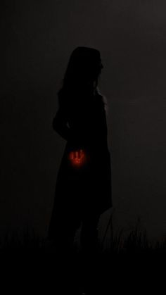 a woman standing in the dark holding an orange light up pumpkin with her face glowing