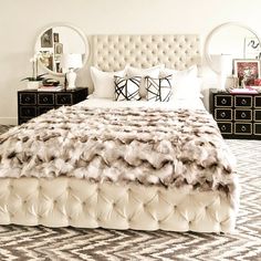 a white bed topped with lots of pillows next to two dressers and a mirror