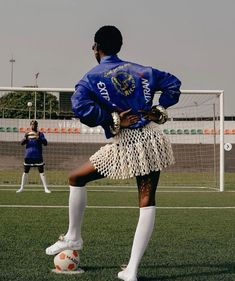 a woman in a blue jacket and white skirt kicking a soccer ball