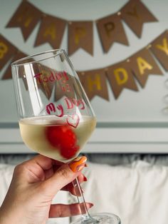 a person holding up a wine glass in front of a happy birthday sign on the wall