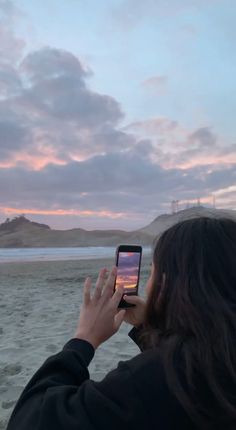 a woman taking a photo with her cell phone on the beach at sunset or dawn