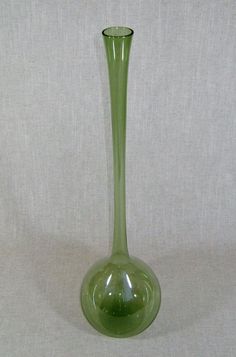 a green glass vase sitting on top of a white cloth covered table next to a wall