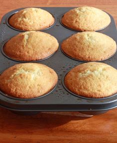 six muffins in a black tray on a wooden counter top, ready to be baked