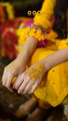 a woman sitting down with yellow powder on her hands and flowers around her arm, all over her body