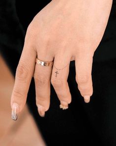 a close up of a person's hand with a cross tattoo on their ring