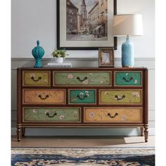 an ornate dresser with painted drawers and flowers on the top, in front of a painting