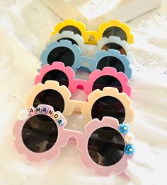 "These sweet, colorful sunglasses for kids are perfect for the beach, a birthday party, or just for fun all year long! Available in six colors, we personalize them with colorful beads with black letters that spell out your child's name or favorite word, and then add a few flowers just for the fun of it! Available only in one size, the typical child size sunglasses. See the measured details below.  Colors: Yellow, gray, blue, dark pink, cream, and light pink UV Lenses - Sturdy Plastic Size: Lens Cute Summer Sunglasses For Birthday, Custom Name Sunglasses For Summer Beach, Custom Name Pink Sunglasses With Adjustable Fit, Pink Sunglasses With Custom Name And Adjustable Fit, Custom Name Sunglasses For Beach In Summer, Summer Birthday Sunglasses With Tinted Lenses, Personalized Sunglasses For Beach, Custom Name Sunglasses As Summer Gift, Whimsical Sunglasses With Uv Protection For Beach