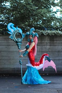 a woman dressed as a mermaid holding a blue and pink dragon spear in her hand