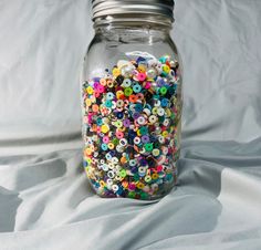 a jar filled with lots of different colored buttons on a white cloth covered tablecloth