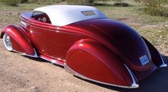 an old red and white car is parked in the dirt