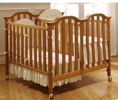 a wooden crib with white bedding in front of a window and wood floor