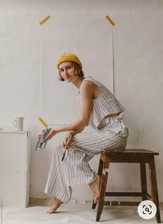 a woman sitting on top of a wooden stool next to a white wall holding an umbrella