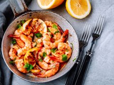 a pan filled with cooked shrimp and garnished with cilantro, parsley and lemon wedges