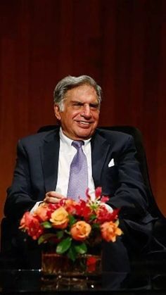 a man in a suit and tie sitting at a table with flowers on the table