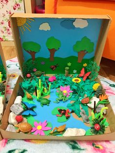 an open cardboard box filled with lots of different types of paper flowers and plants on top of a bed