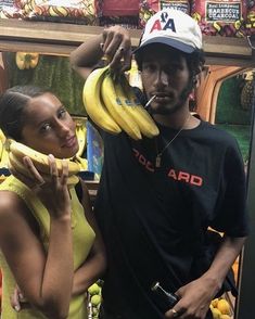 a man and woman standing next to each other with bananas in front of their faces