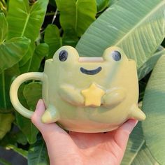 a hand holding a green frog mug with a yellow star on it's face