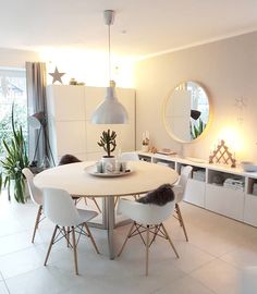 a dining room with white chairs and a round table in the center, surrounded by potted plants