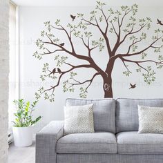 a living room with a gray couch and tree wall decal on the wall behind it