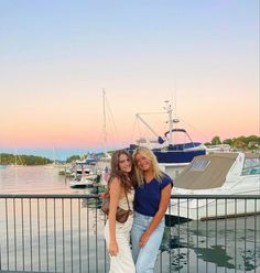 two women standing next to each other in front of a marina with boats on the water