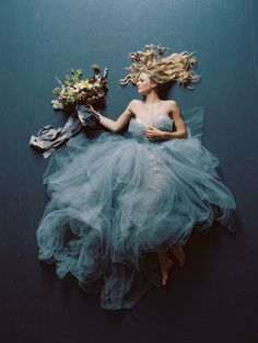 a woman in a blue dress laying on the ground with her hair blowing in the wind